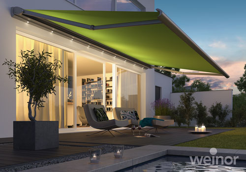 Grüne Markise mit LED-Beleuchtung ausgefahren über einer Terrasse mit Pool.
